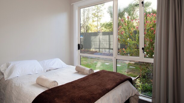 Un dormitorio con un ventanal grande, una cama con ropa blanca y un plaid marrón.