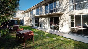 Una casa moderna de dos pisos con amplios ventanales, un balcón y un césped cuidado con mobiliario exterior.