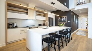 A modern kitchen with a central island, bar stools, and a dining area. - The Stella, minutes to the village/free shuttle (Mont-Tremblant)