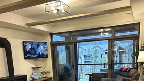 Una sala de estar moderna con chimenea, asientos cómodos, un televisor y un gran ventanal corredera que da a un balcón.