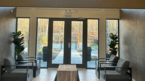 Un vestíbulo amplio con techo alto, ventanas grandes y una zona de estar central con dos sofás y una mesa de centro.
