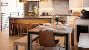 Een moderne keuken met een centraal eiland, hanglampen en een eethoek met een houten tafel en stoelen.