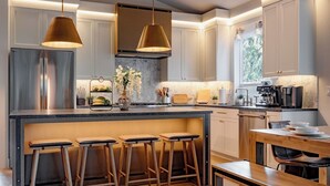 Een moderne keuken met een centraal eiland, barstoelen, roestvrijstalen apparatuur en hanglampen.