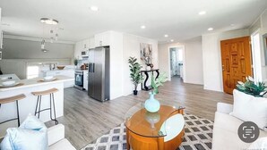A modern kitchen with white cabinets, a stainless steel refrigerator, and a bar area with stools.