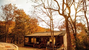 Eine rustikale Holzhütte mit Veranda, umgeben von Bäumen im Herbstlaub.