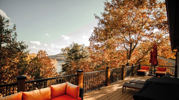 Eine Holzterrasse mit Sitzgelegenheit, Blick auf einen See und Herbstlaub.