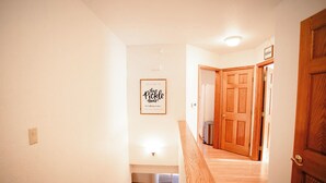 Ein Flur mit einer Holztreppe, einem begrüßungsschild im Bilderrahmen und Holztüren.