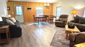 A living room with a wooden floor, a dining area with a wooden table and chairs, and a sofa.