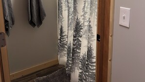 A bathroom with a shower curtain featuring a forest pattern, a towel rack with towels, and a wooden floor.