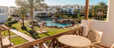 A balcony with a view of a swimming pool, palm trees, and a building with arched windows.