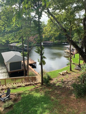 A lakeside property with docked boats, a covered deck area, and a grassy lawn with outdoor furniture. - Blue Heron Hideaway on beautiful Lake Sinclair.  (Eatonton)