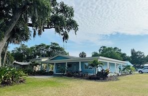 A two-story house with a covered porch, surrounded by lush greenery and trees.