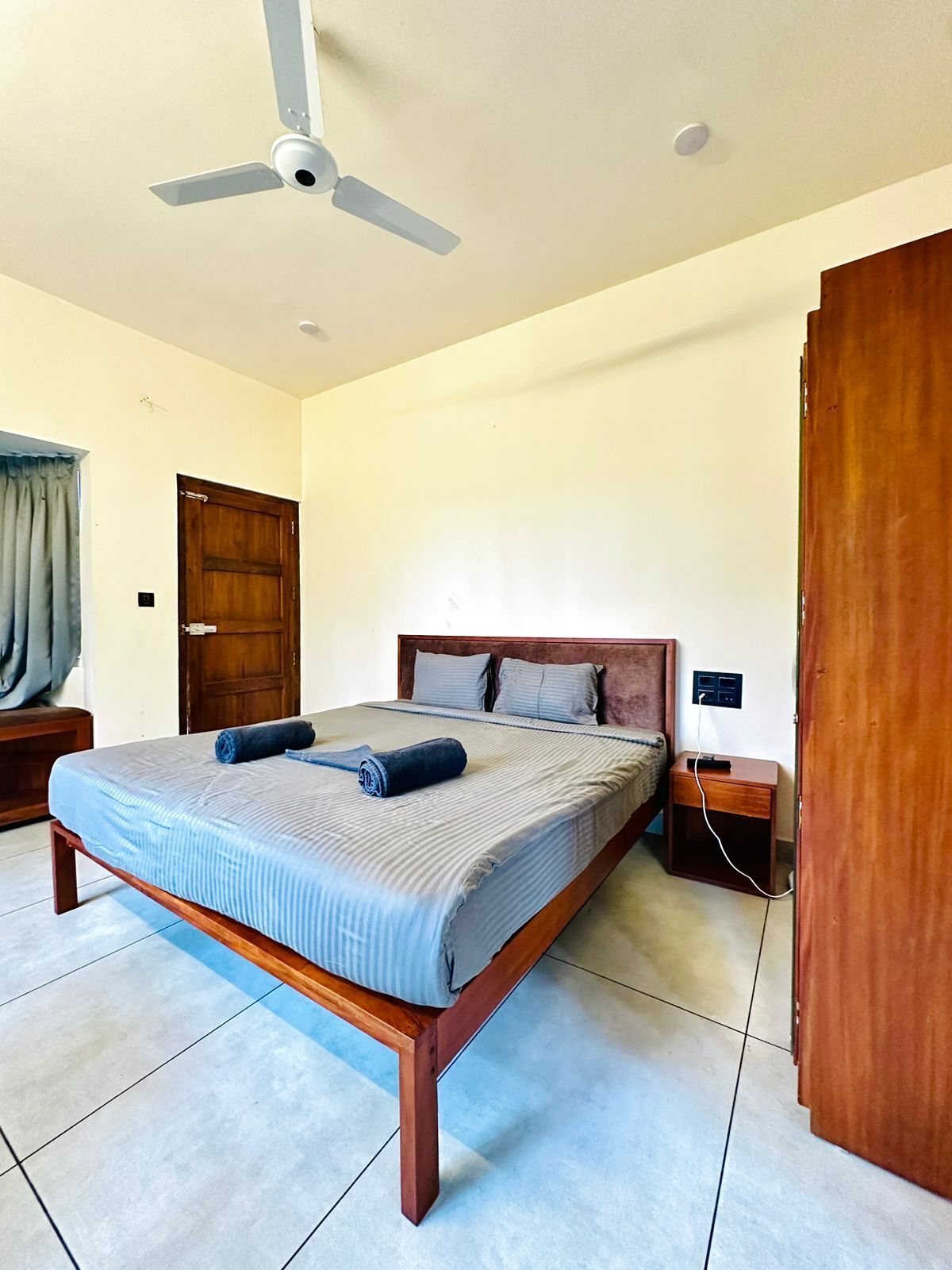 A bedroom with a bed, wooden headboard, a ceiling fan, a nightstand, and a door.
