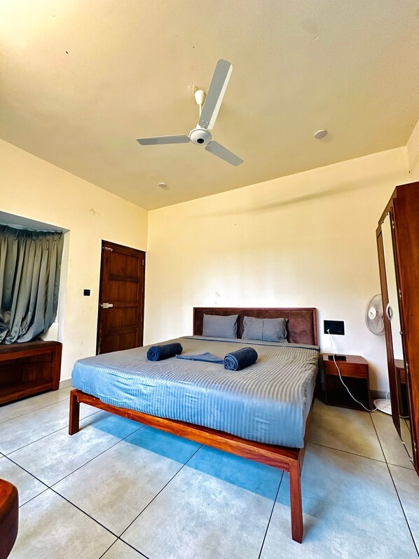 Un dormitorio con cama, cabecero de madera, ventilador de techo y mesita de noche con lámpara.
