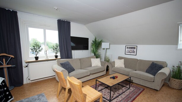 Ein Wohnzimmer mit zwei Sofas, einem Couchtisch, einem Sessel, einer Heizung und einem Fenster mit Vorhängen.