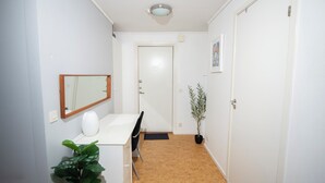 Ein schmaler Korridor mit einer weißen Tür am Ende, einem kleinen Tisch mit Stuhl, einer Topfpflanze und einem Spiegel an der Wand.