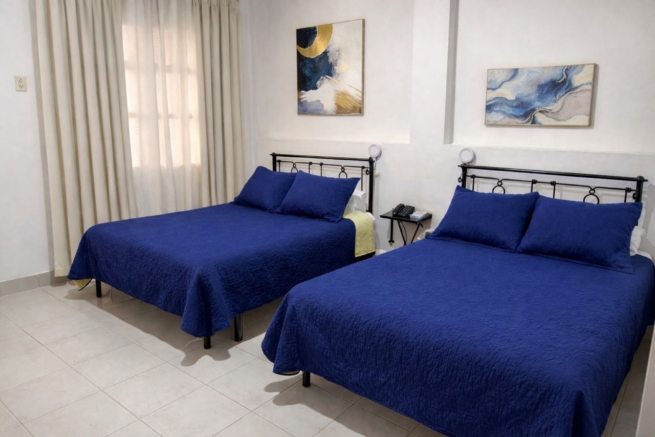 Twee enkele bedden met blauw beddengoed, een nachtkastje met een telefoon, en abstracte kunst aan de wanden.