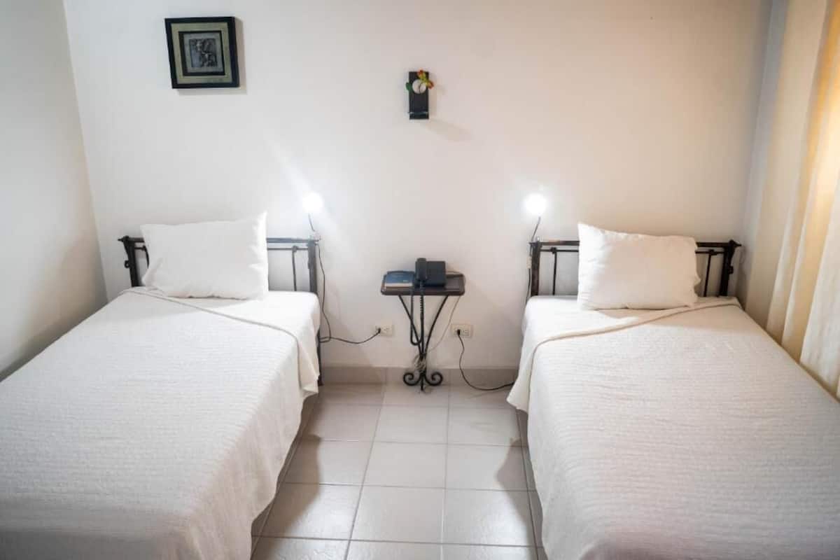 A twin room with two beds, a small table, and a wall-mounted light fixture.