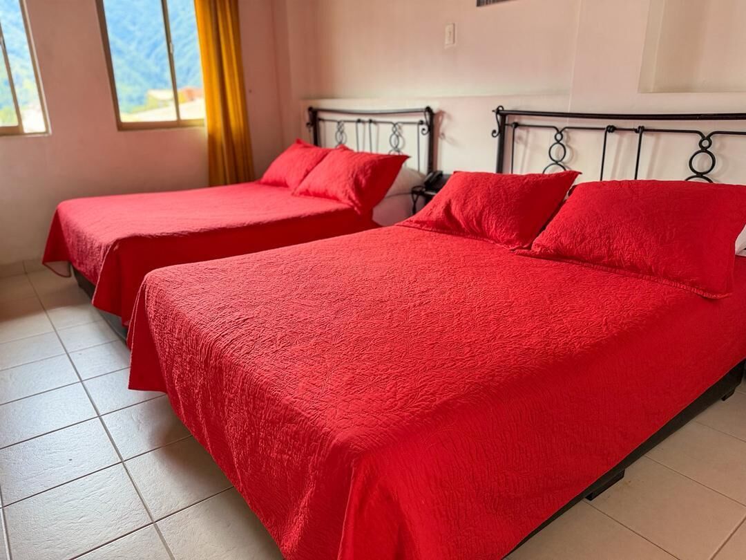 Two single beds with red bedding, a window with yellow curtains, and a tiled floor.