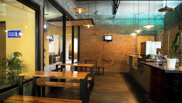 A restaurant interior with wooden tables and benches, brick walls, and hanging pendant lights. - Hotel Plaza CA (Merida)