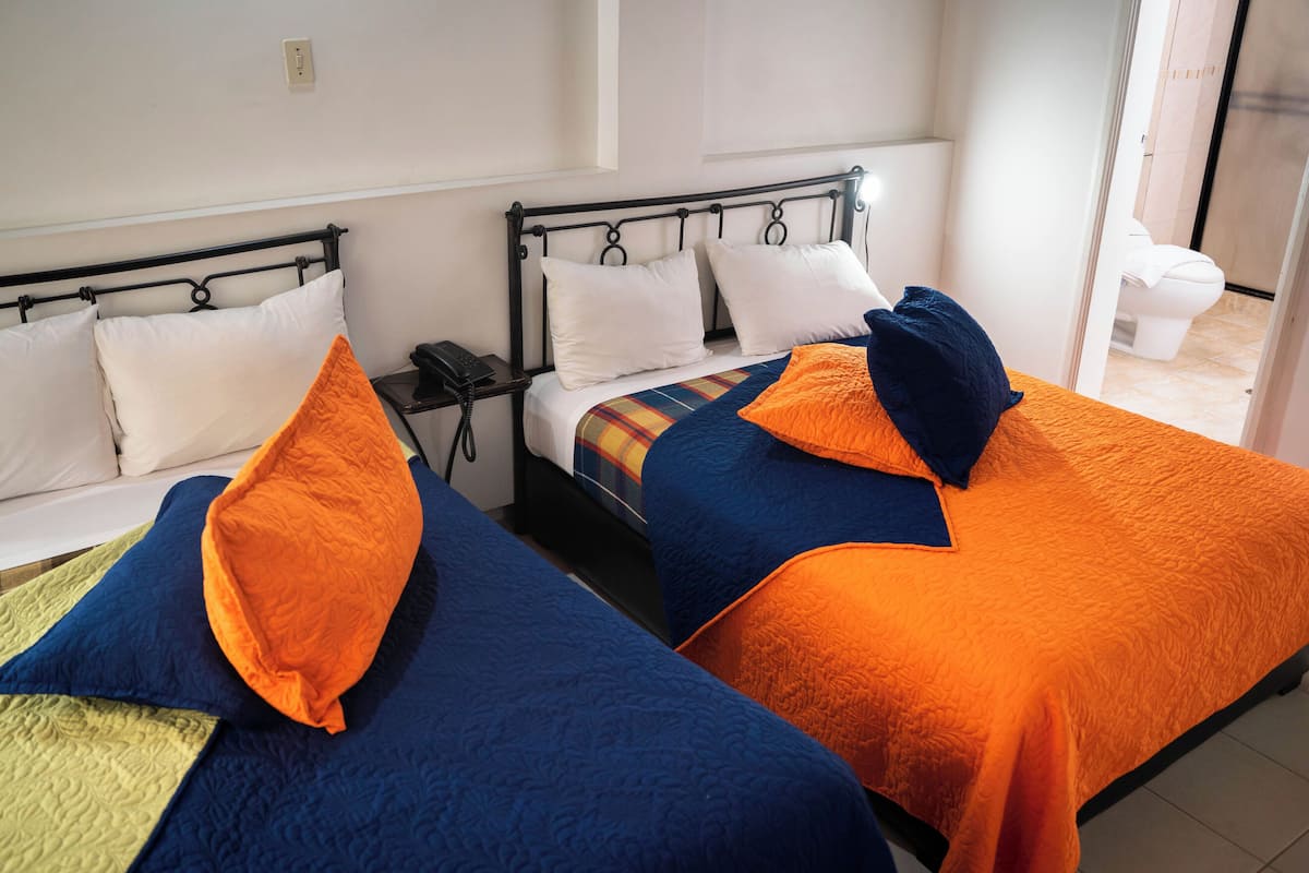 A hotel room with two beds, each with a different colored bedspread and pillows. There is a nightstand with a phone and a lamp between the beds.