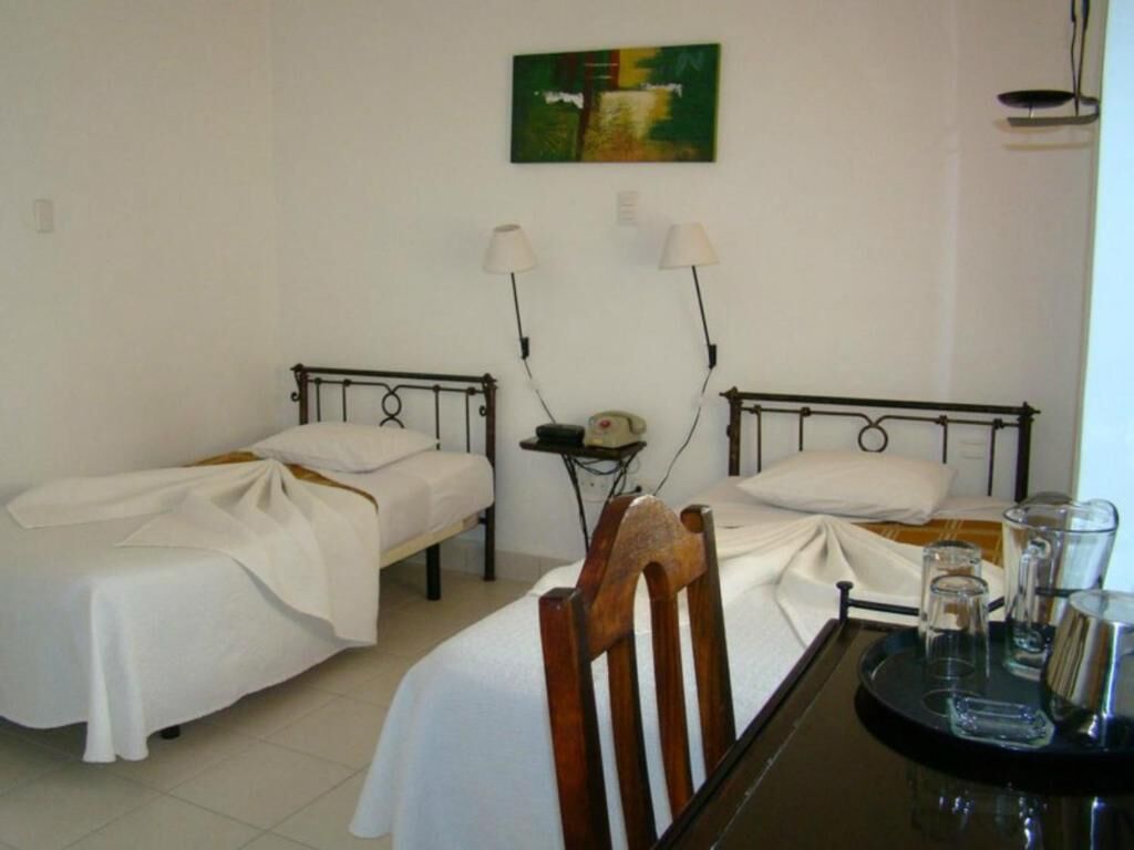 A room with two single beds, a small table with glasses, and a painting on the wall.