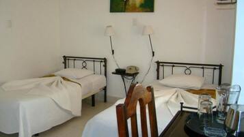 A room with two single beds, a small table with glasses, and a painting on the wall.