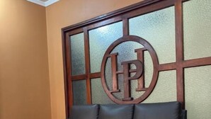 A dark leather sofa with a matching ottoman, positioned against a wall with a decorative wooden panel featuring a circular emblem. - Hotel Plaza CA (Merida)