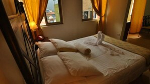 A hotel room with a bed, curtains, a nightstand, and a window with a view of buildings. - Hotel Plaza CA (Merida)