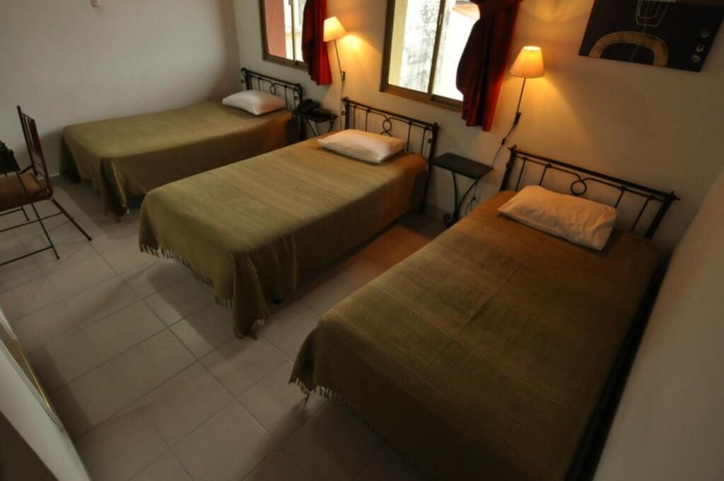 Una habitación con tres camas individuales, cada una con cabecera y mesita de noche.