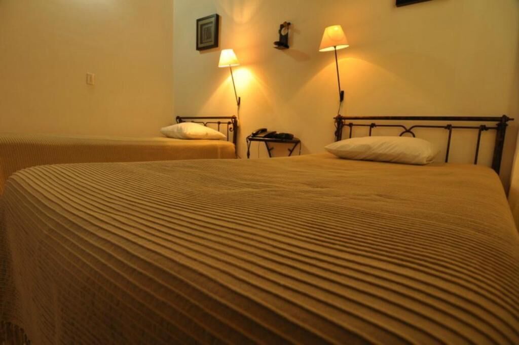 A hotel room with two beds, each with a headboard and a bedside table with a lamp.