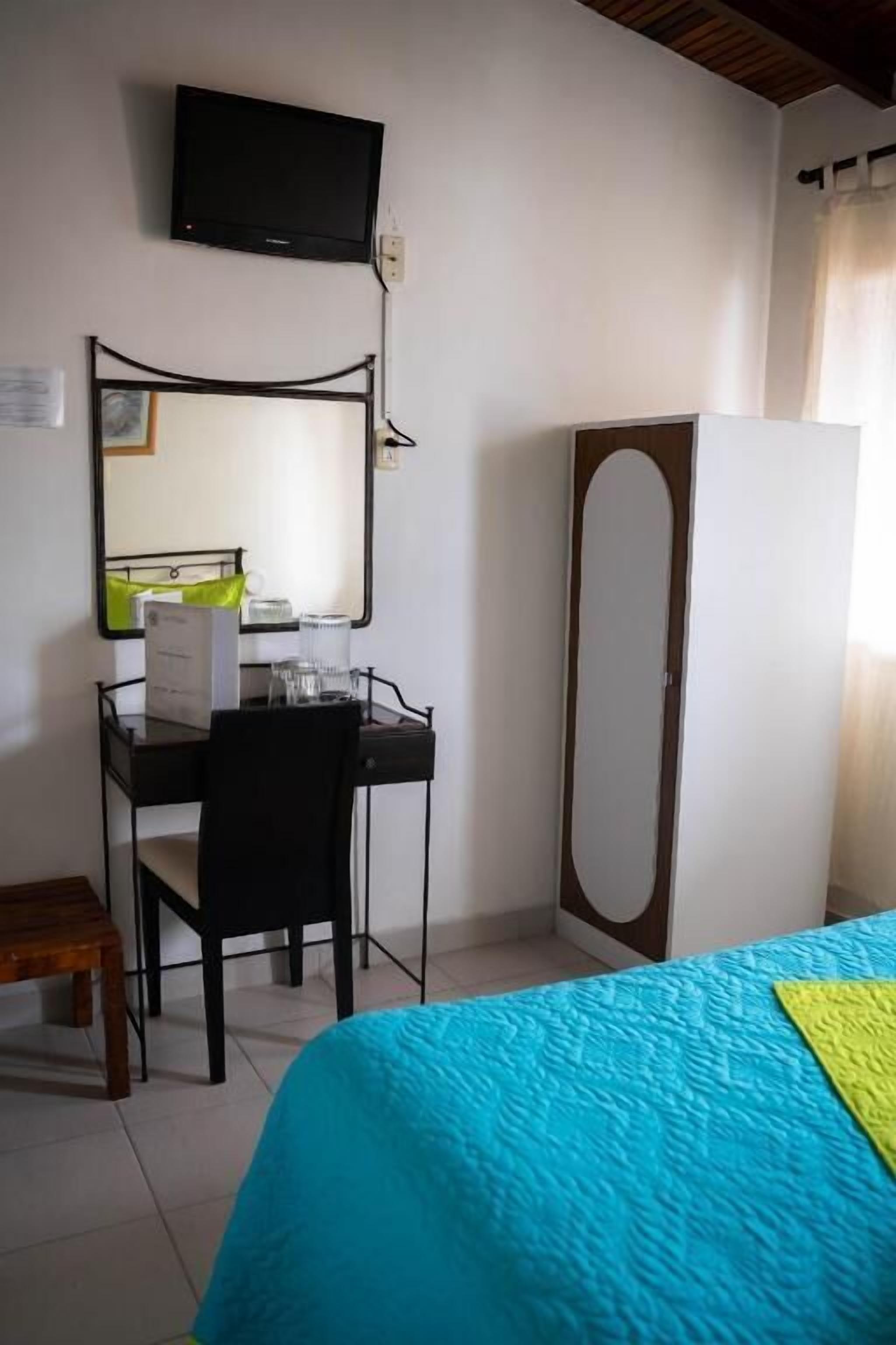 A bedroom with a bed, a desk with a chair, a mirror, and a television on the wall.