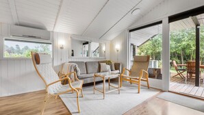 Une pièce chaleureuse avec un plancher en bois, un canapé et deux fauteuils. Il y a une fenêtre et une porte qui donne sur l’extérieur.