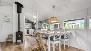 Une cuisine moderne avec des meubles blancs, une table à manger en bois avec des chaises, une grande fenêtre et une vue sur la verdure à l’extérieur.