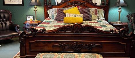 Una cama tradicional con dosel y cuatro columnas, un banco al pie y una alfombra estampada.