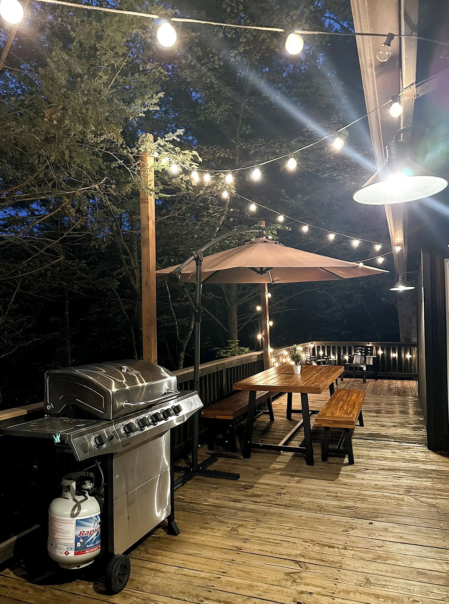 Een terras buiten met een barbecue, tafels en lichtslingers.