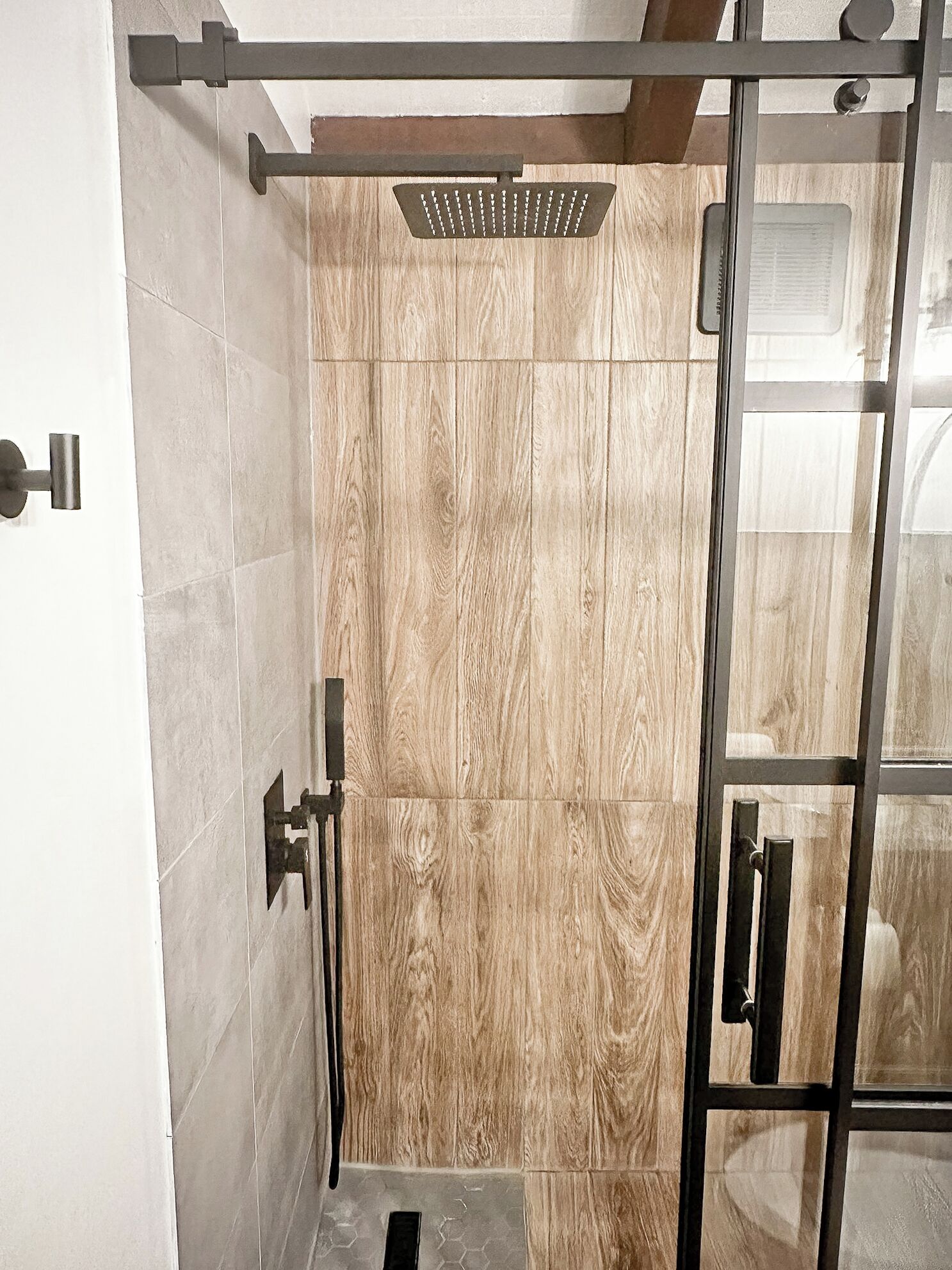 A modern shower with a wooden panel wall, a glass door, and a metal handle.