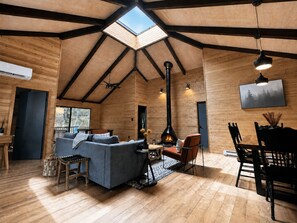 A spacious room with a high ceiling, a skylight, a fireplace, and a dining area.