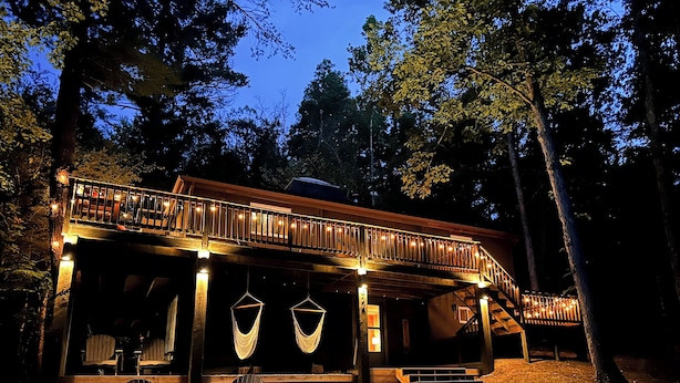Une cabane en bois dotée d’un porche couvert, de sièges d’extérieur et de hamacs suspendus.