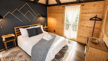 Een slaapkamer met een bed, nachtkastjes, een hanglamp, een raam met gordijnen, een houten dressoir en een kamerbreed vloerkleed.