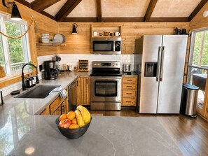 A modern kitchen with stainless steel appliances, wooden cabinets, and a large window. - CasaSOL: Stylish Mountain Cabin with Game Room, Trails and Fire Pit Nights (Basye)