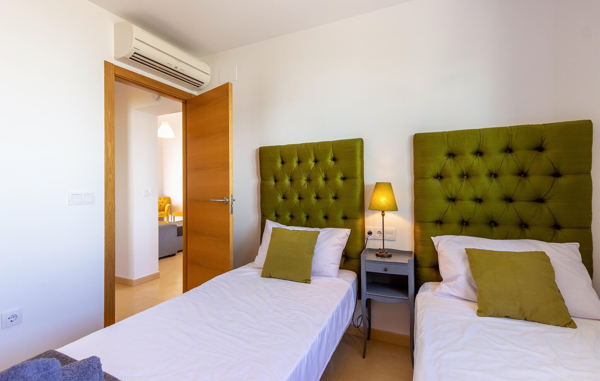 Une chambre d’hôtel avec deux lits, chacun doté d’une tête de lit verte à motifs capitonnés, de draps blancs et d’une petite table de chevet avec une lampe.