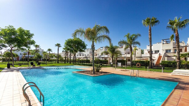A swimming pool with a tiled deck, surrounded by palm trees and modern buildings.