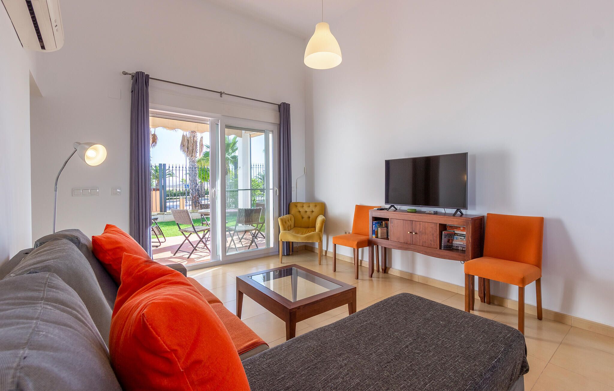 Un salon comprenant un canapé, deux fauteuils, une table basse, un téléviseur et une porte-fenêtre coulissante donnant sur un espace extérieur.