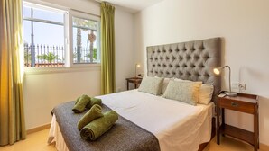 A hotel room with a large bed, a window with curtains, and a view of palm trees.