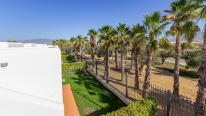 A white building with a paved pathway, surrounded by palm trees and a fence.