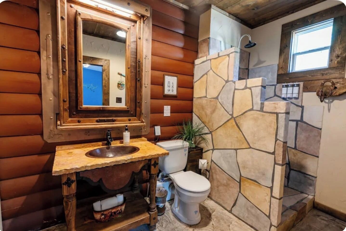 A rustic bathroom with a stone shower, wooden walls, and a large mirror.