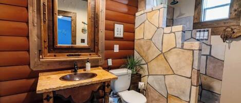 A rustic bathroom with a stone shower, wooden walls, and a large mirror.