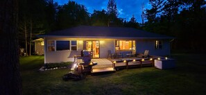 A house with a covered patio, outdoor seating, and a well-lit interior. - Sunny Side U.P.: Lake Michigan Fall Getaway | Hot Tub + Fireplace + Fire Pit (Manistique)