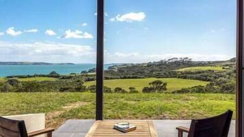 A terrace with a table and chairs overlooking a coastal landscape with rolling hills and a body of water.